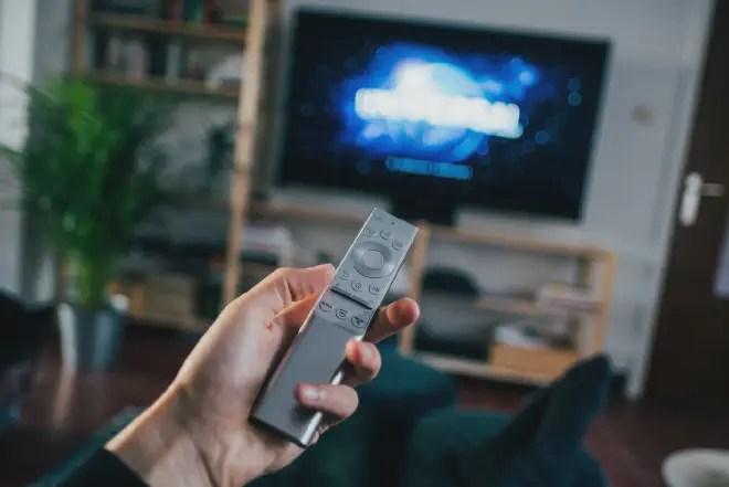 A hand holding a Firestick remote with the text How to Restart Firestick Remote